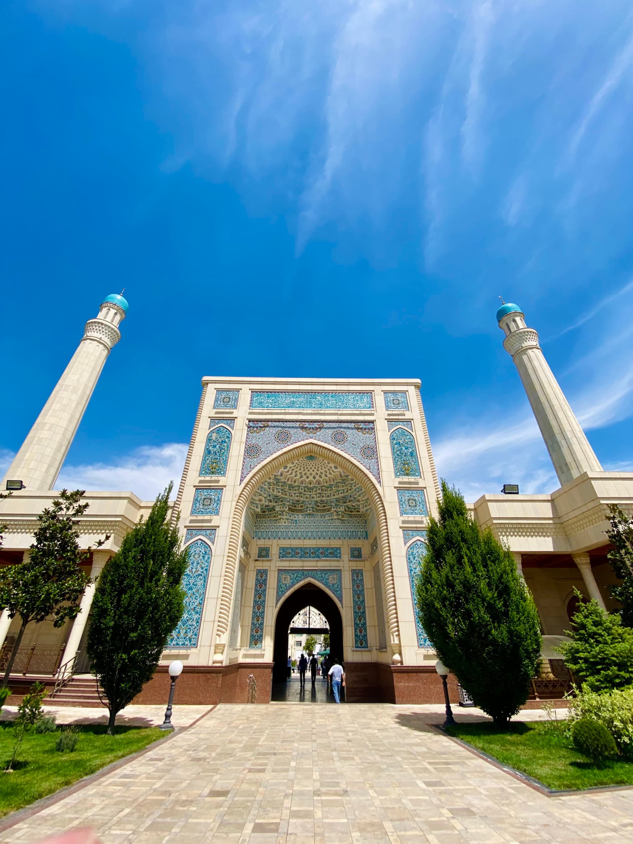 A stunning mosque entrance under a vibrant blue sky, with intricate tilework and lush greenery, exuding tranquility and architectural beauty