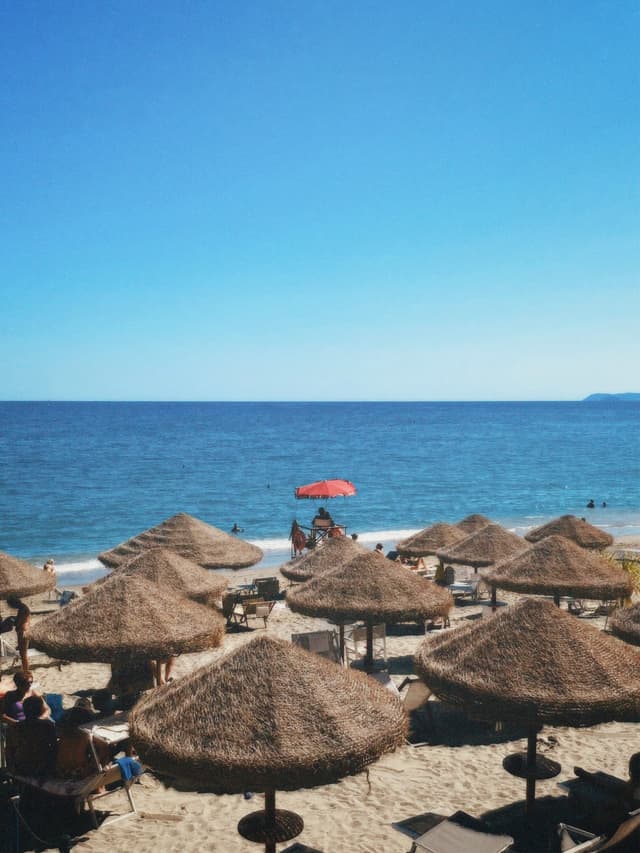 A serene beach scene with straw umbrellas, calm turquoise waters, and a clear blue sky, evoking relaxation and vacation vibes