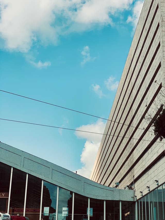 Sunny urban scene with modern buildings, clear blue sky, and soft clouds, evoking a calm, pleasant atmosphere