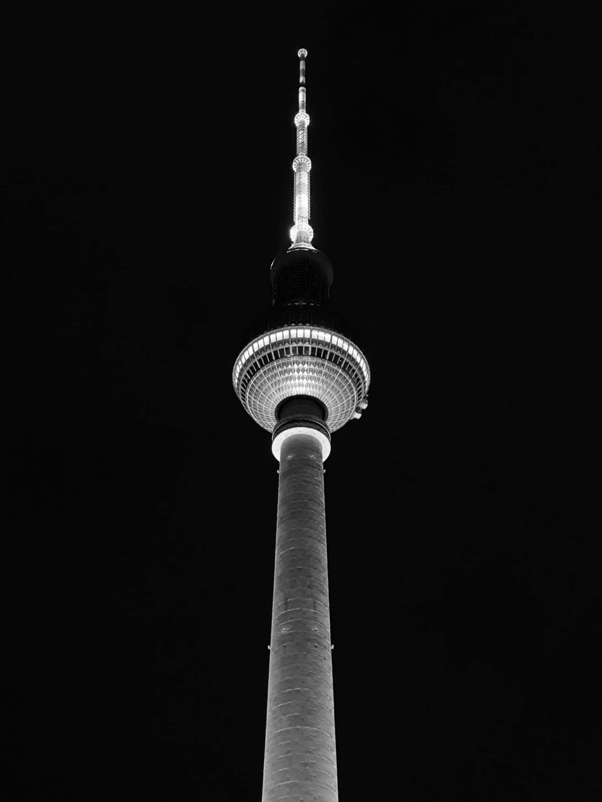 A striking black and white image of Berlin's Fernsehturm illuminated against a dark sky, evoking a sense of mystery and urban elegance