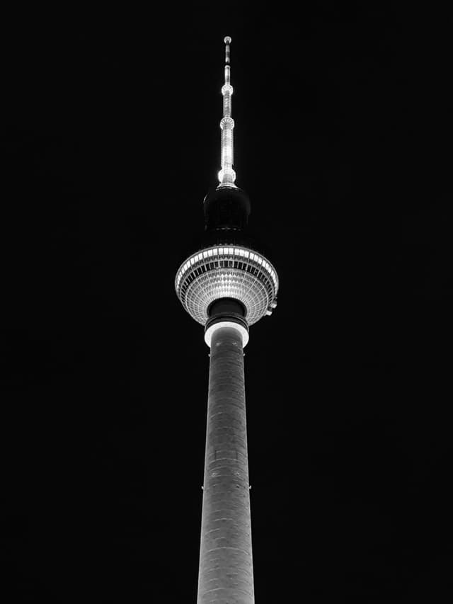 A striking black and white image of Berlin's Fernsehturm illuminated against a dark sky, evoking a sense of mystery and urban elegance