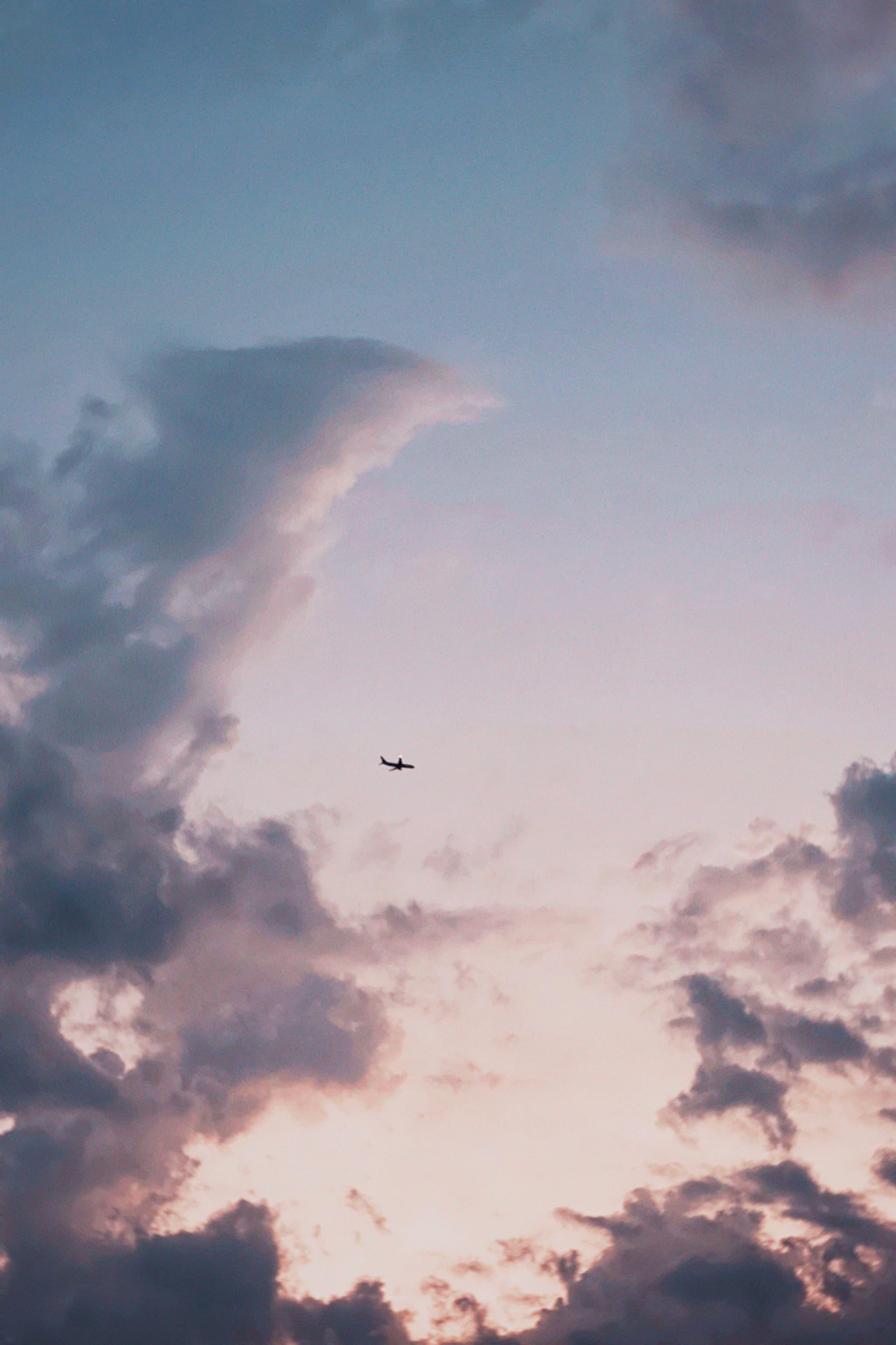 A serene sky scene with dramatic clouds and a small airplane flying at sunrise or sunset, capturing a tranquil and peaceful moment