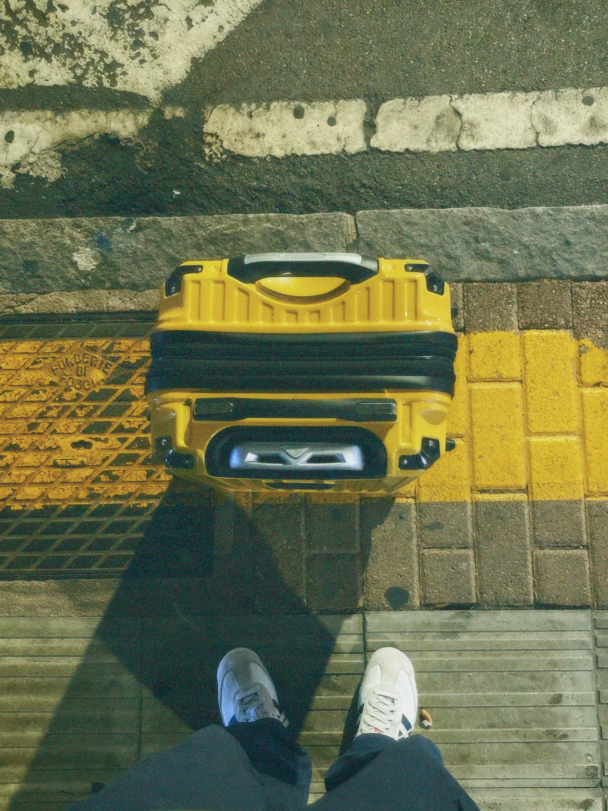 A yellow suitcase rests on a textured pavement, illuminated by soft street lighting, creating a serene, urban evening atmosphere