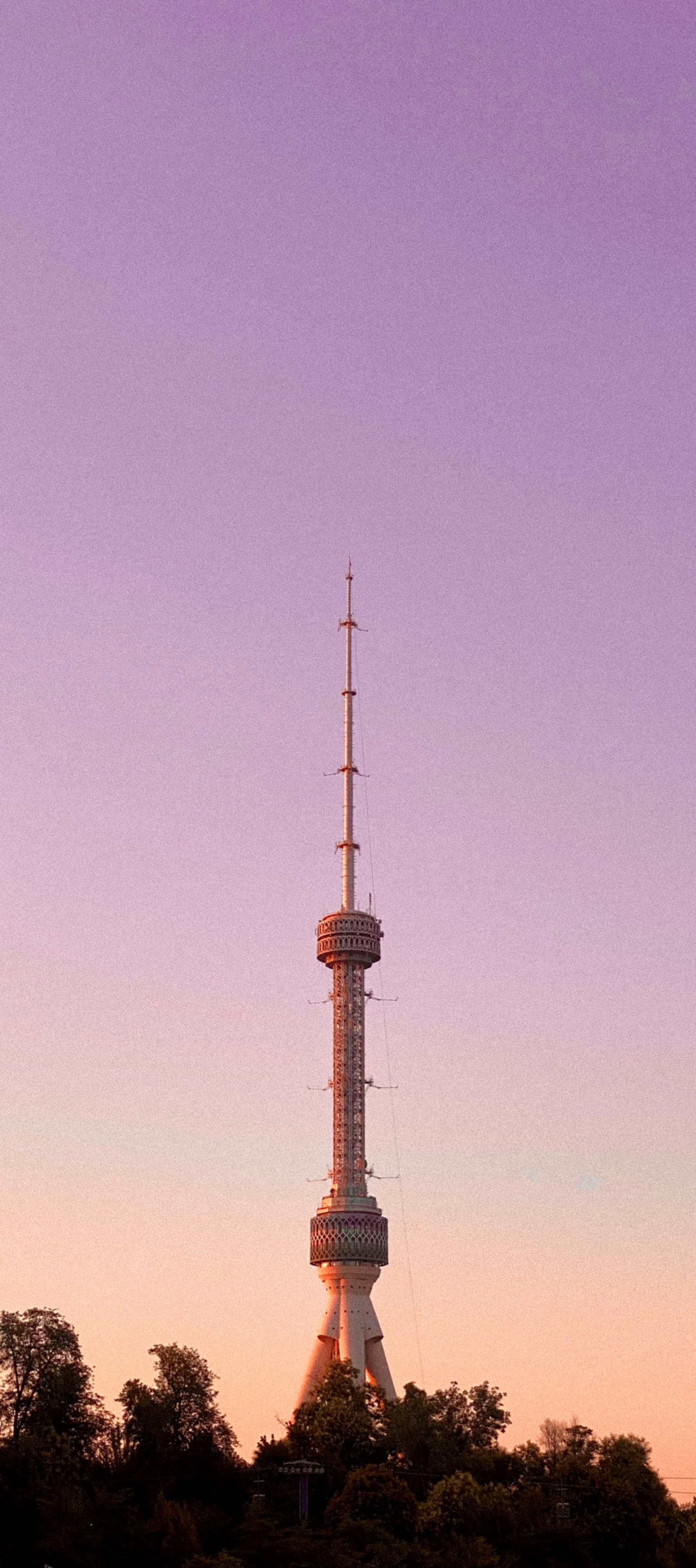 A serene sunset frames a tall TV tower, casting a warm orange hue over the urban landscape