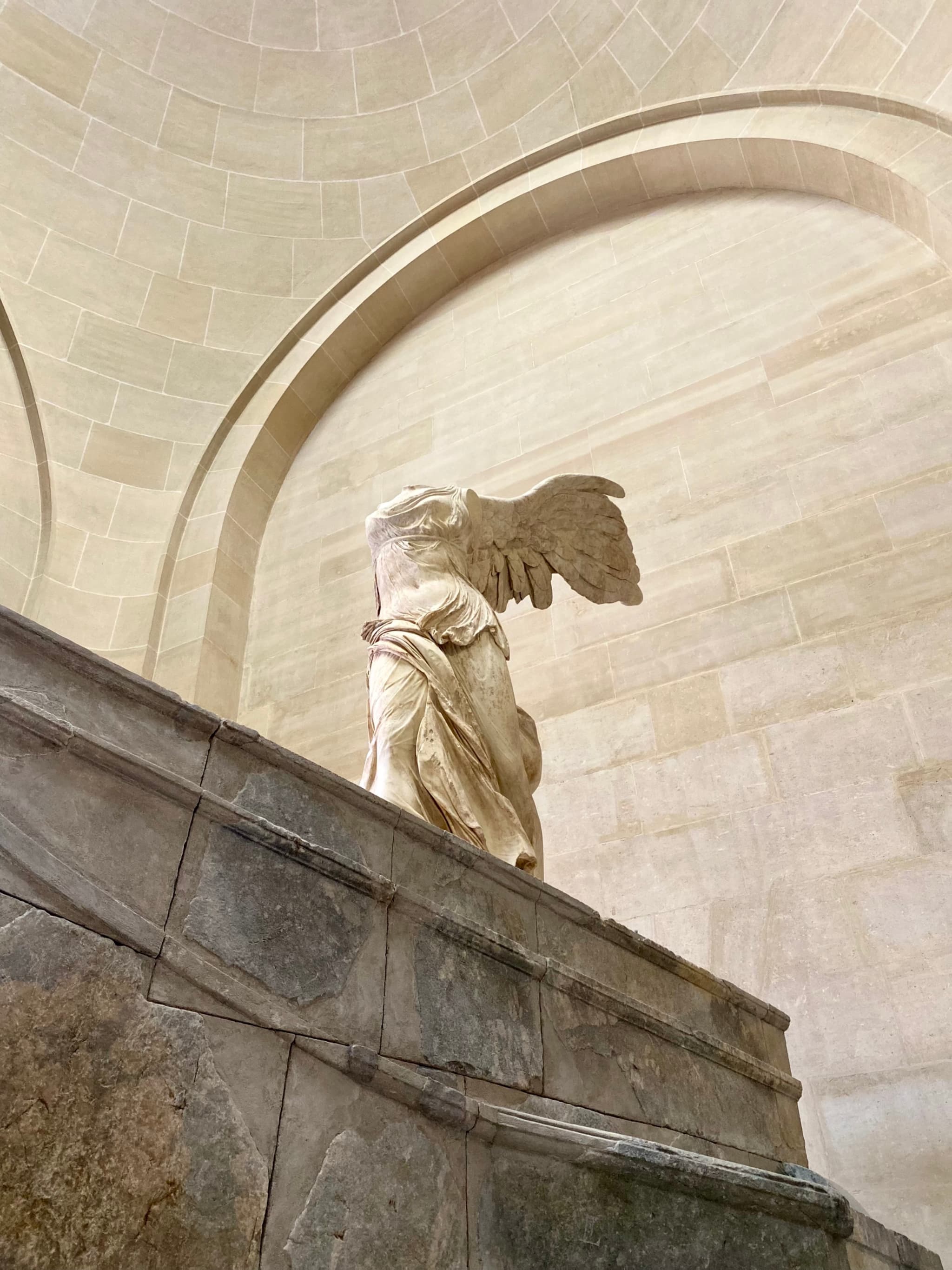 The Winged Victory of Samothrace, illuminated softly, rests atop a marble pedestal within the Louvre Museum's serene, classical setting