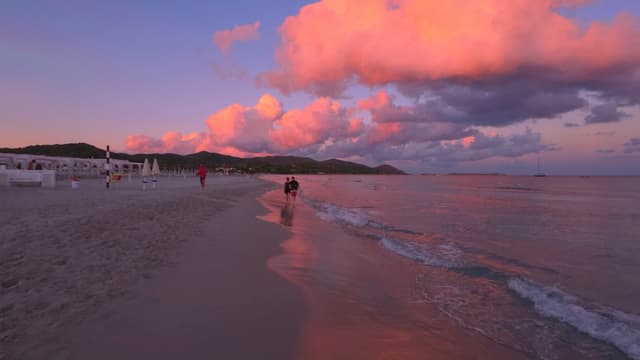 Golden hour beach scene with pink and orange clouds, soft sand, gentle waves, and sunset hues creating a serene and picturesque atmosphere
