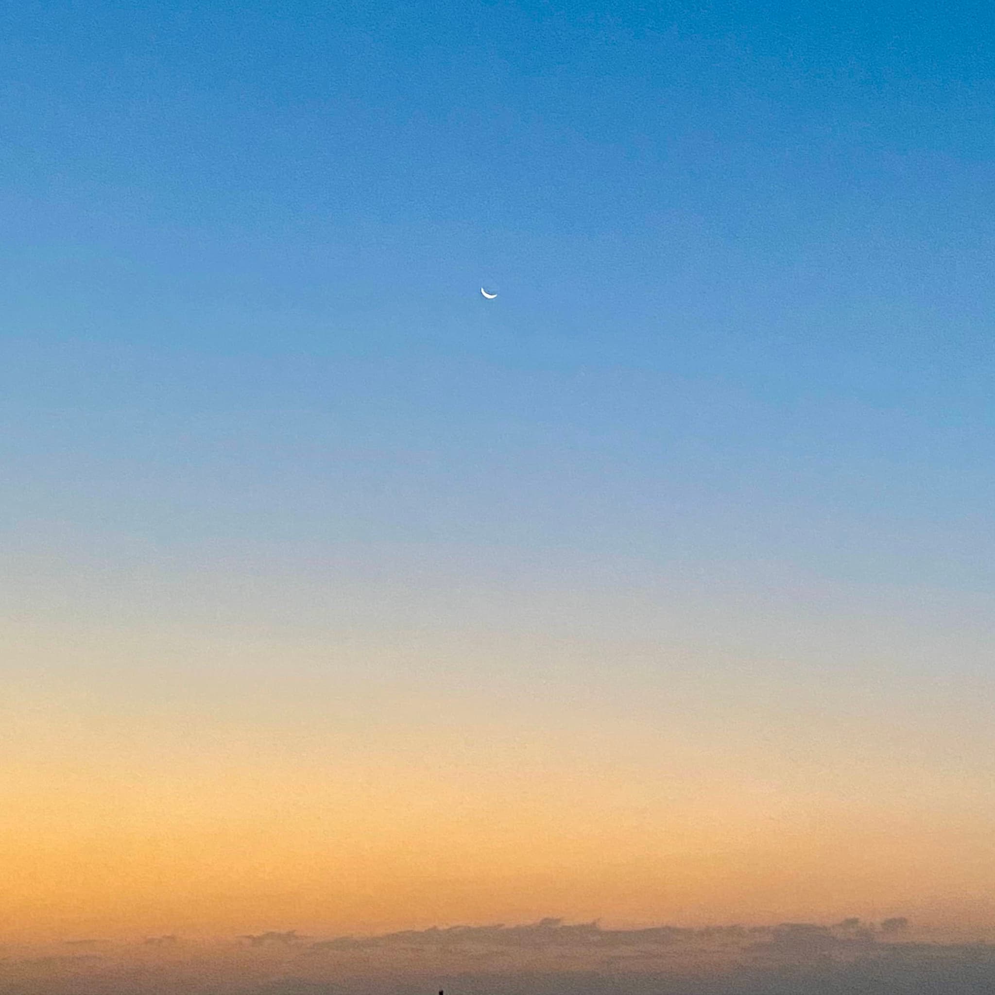 A serene sunset sky with a soft gradient of warm orange to deep blue, featuring a bright white crescent moon