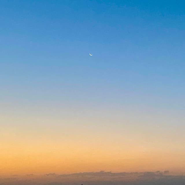 A serene sunset sky with a soft gradient of warm orange to deep blue, featuring a bright white crescent moon