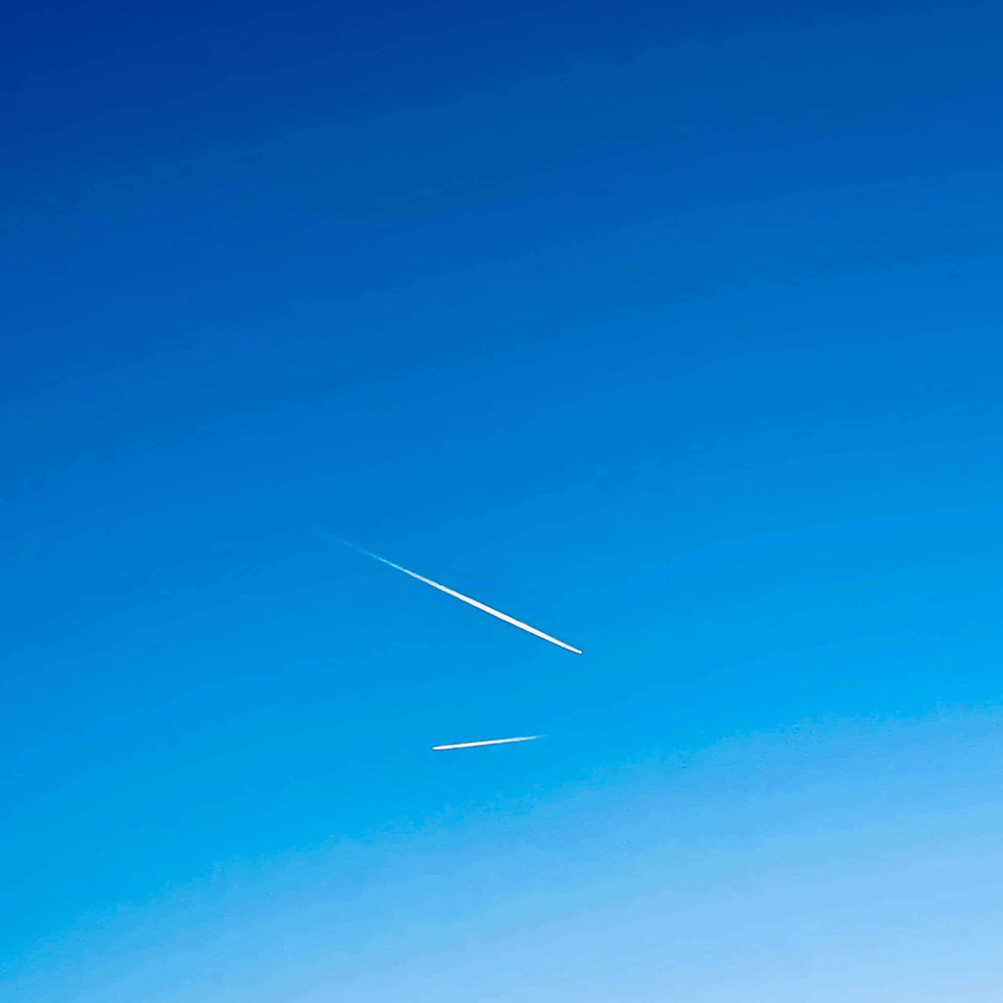 Two air traffic contrails stretch across a serene, clear blue sky, emphasizing the vastness and tranquility of a high-altitude view