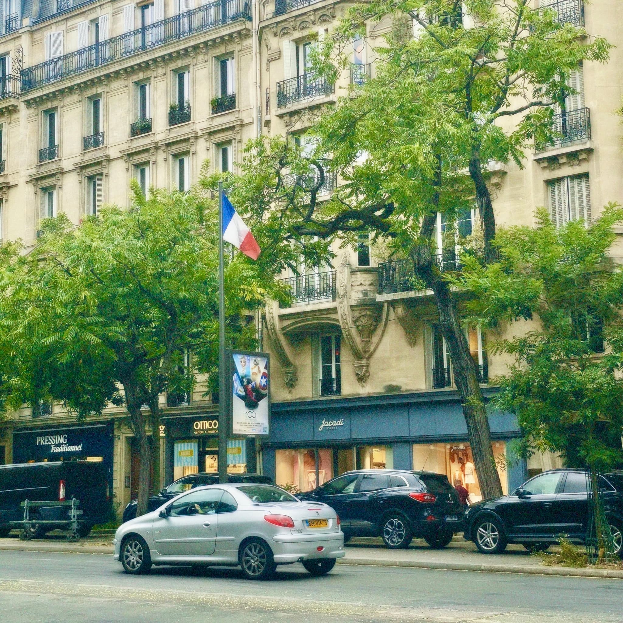 A serene daytime Parisian street with parked cars, greenery, and classic architecture, evoking a calm and timeless European atmosphere