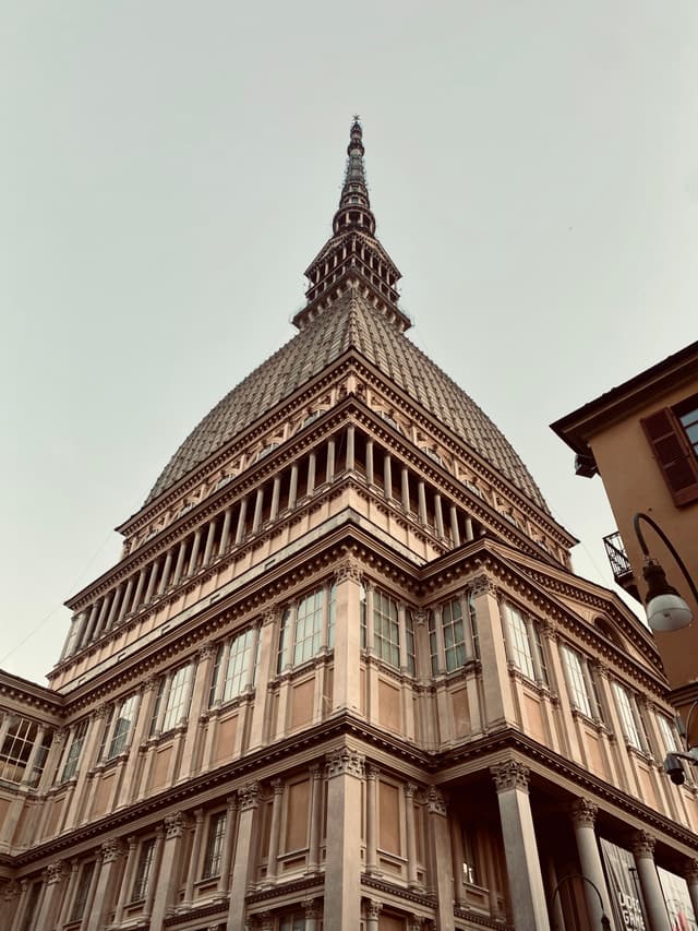 A historic church, Mole Antonelliana, stands majestically against a clear sky in Turin, Italy, with warm lighting and a serene, inviting atmosphere