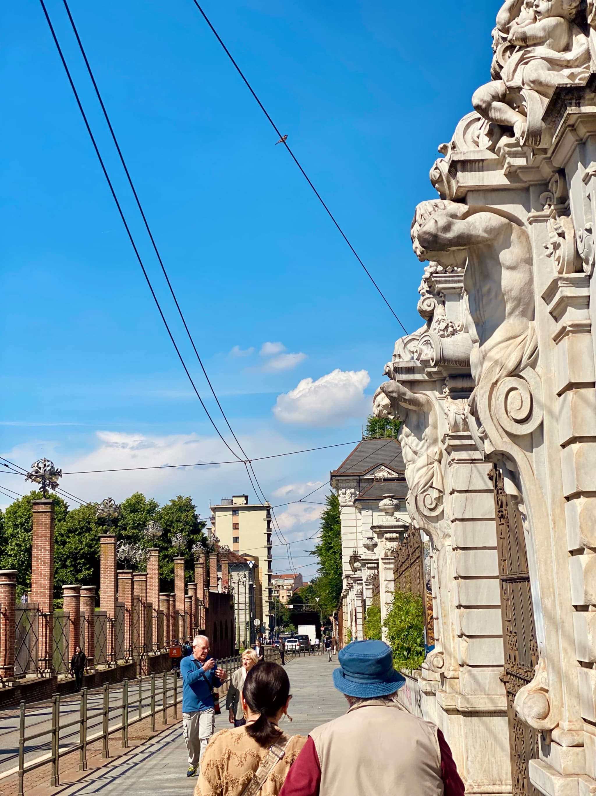 A vibrant street scene in Milan, Italy, with ornate gate, pedestrians, and historic buildings under a clear blue sky
