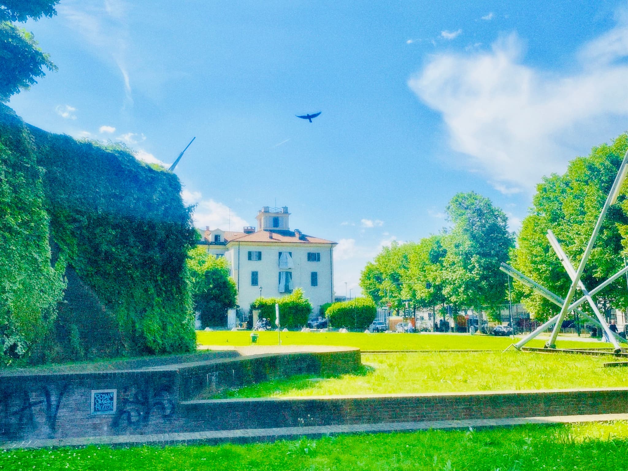 A serene garden with a white building, lush greenery, and a clear blue sky, bathed in natural sunlight, evokes a tranquil, peaceful mood