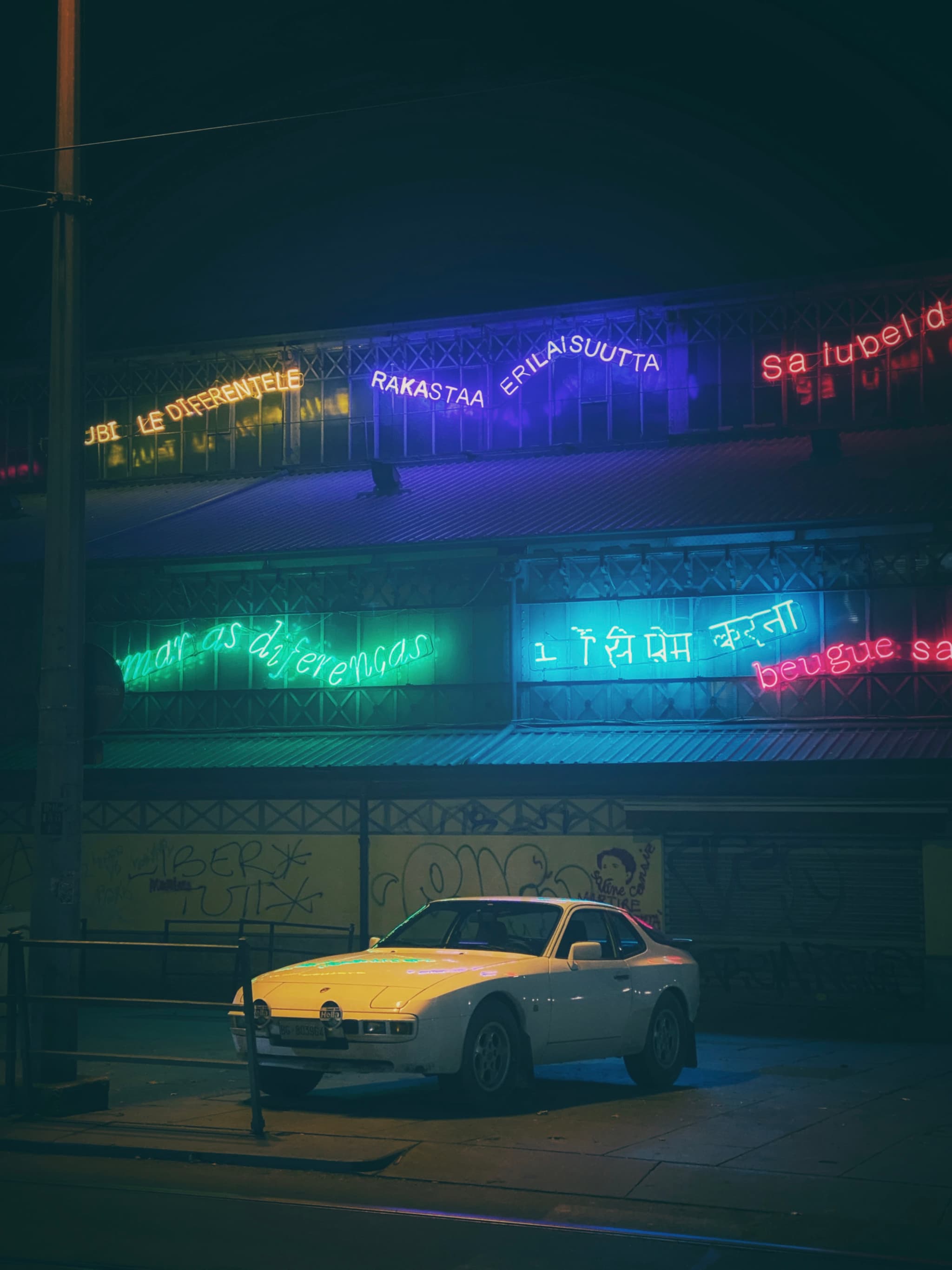 A vintage Porsche 911 glows under neon lights, encapsulating a moody, urban nighttime scene with graffiti art and illuminated signs in the background