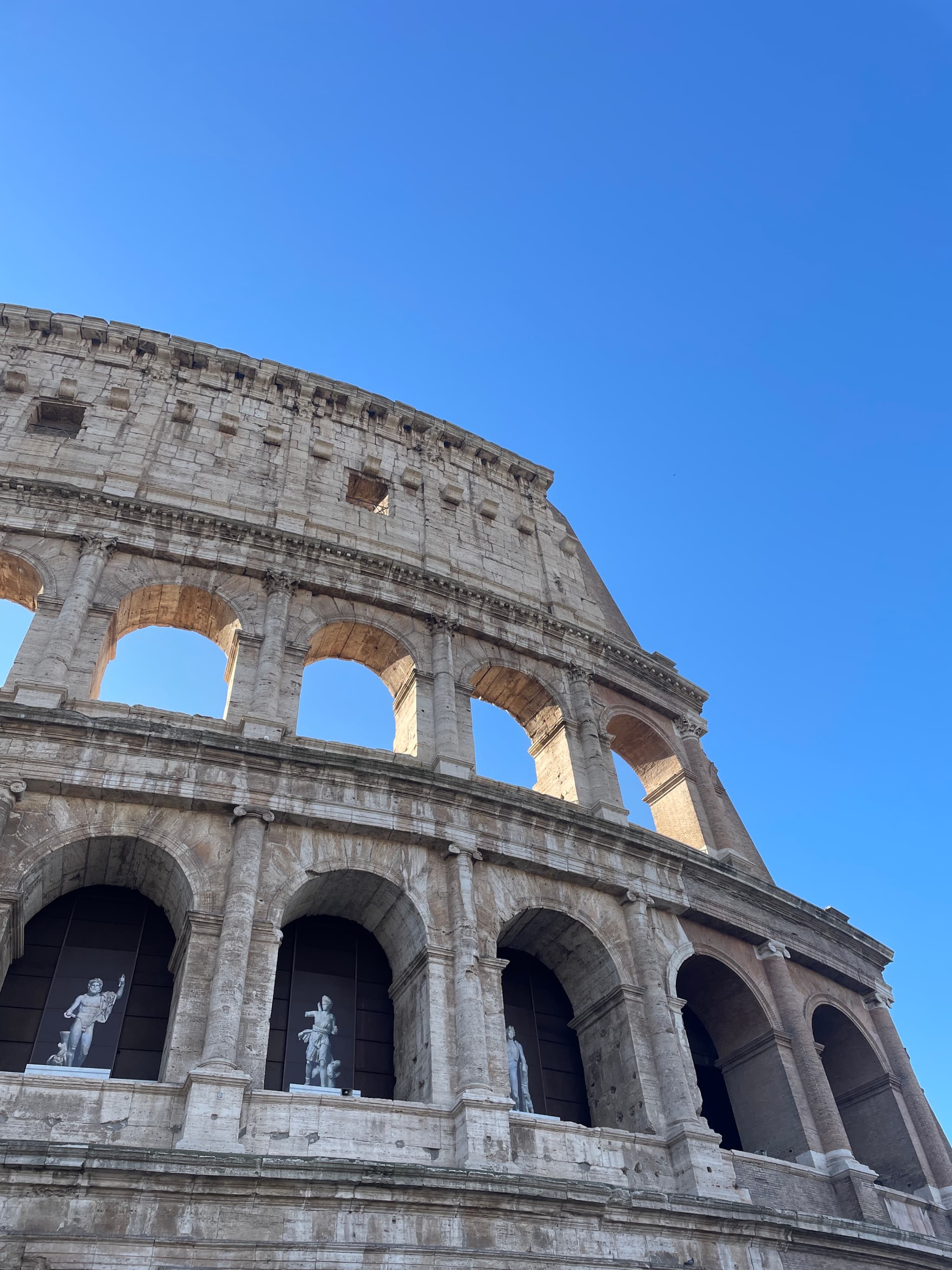 The ancient Colosseum stands majestically against a vibrant blue sky, bathed in soft, natural sunlight, evoking a sense of historical grandeur and timeless beauty