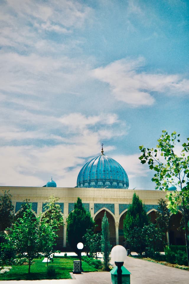 A serene blue-tiled mosque under a bright sky and lush greenery, evoking tranquility and cultural richness