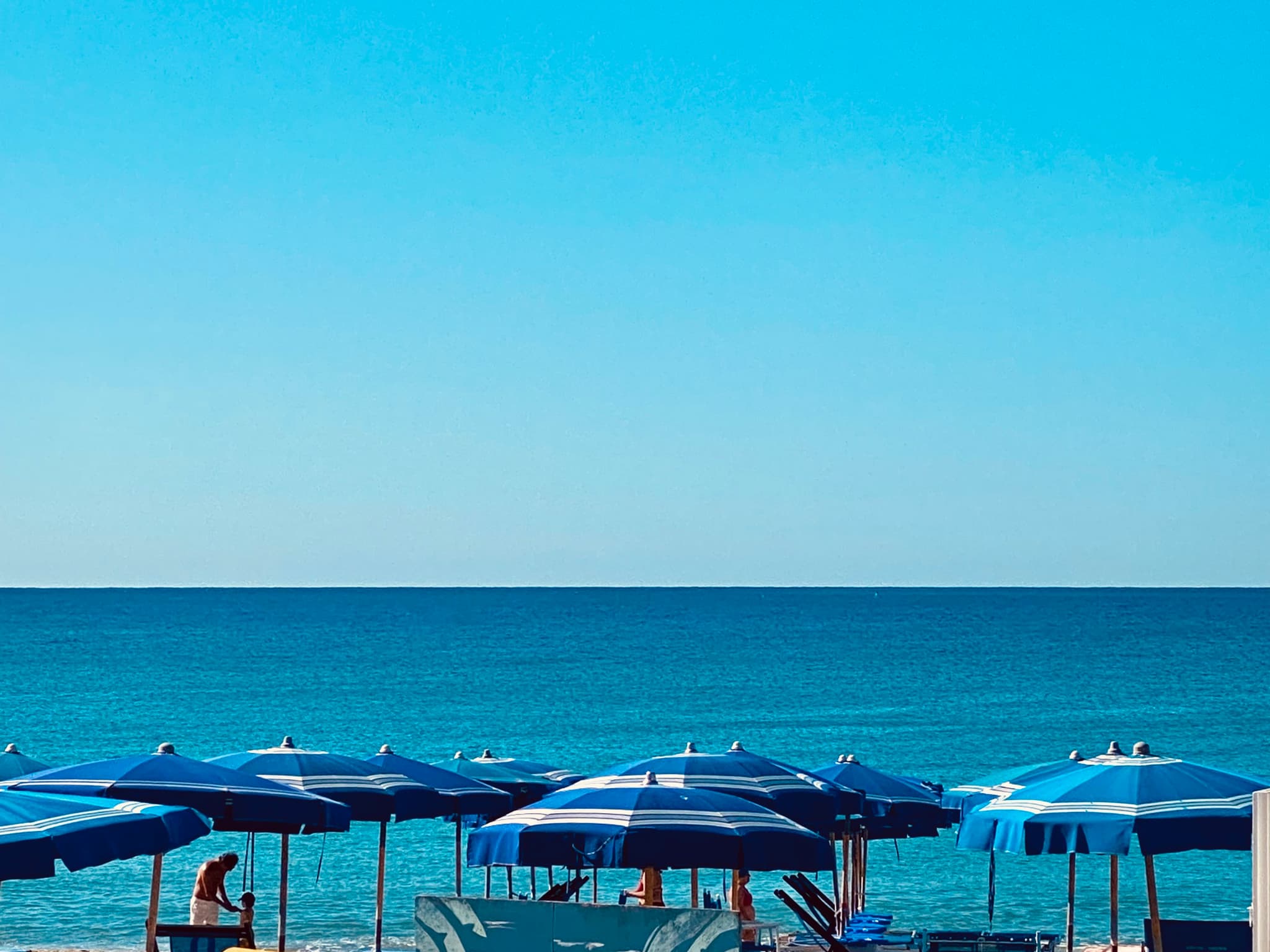 A serene beach scene with vibrant blue umbrellas and calm ocean under a clear sky, evoking relaxation and tranquility