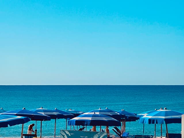 A serene beach scene with vibrant blue umbrellas and calm ocean under a clear sky, evoking relaxation and tranquility