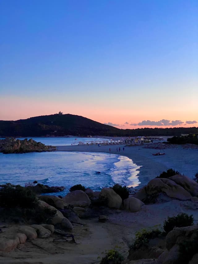 A serene sunset at a beach with calm waters, soft sand, and silhouetted dunes, creating a tranquil coastal atmosphere