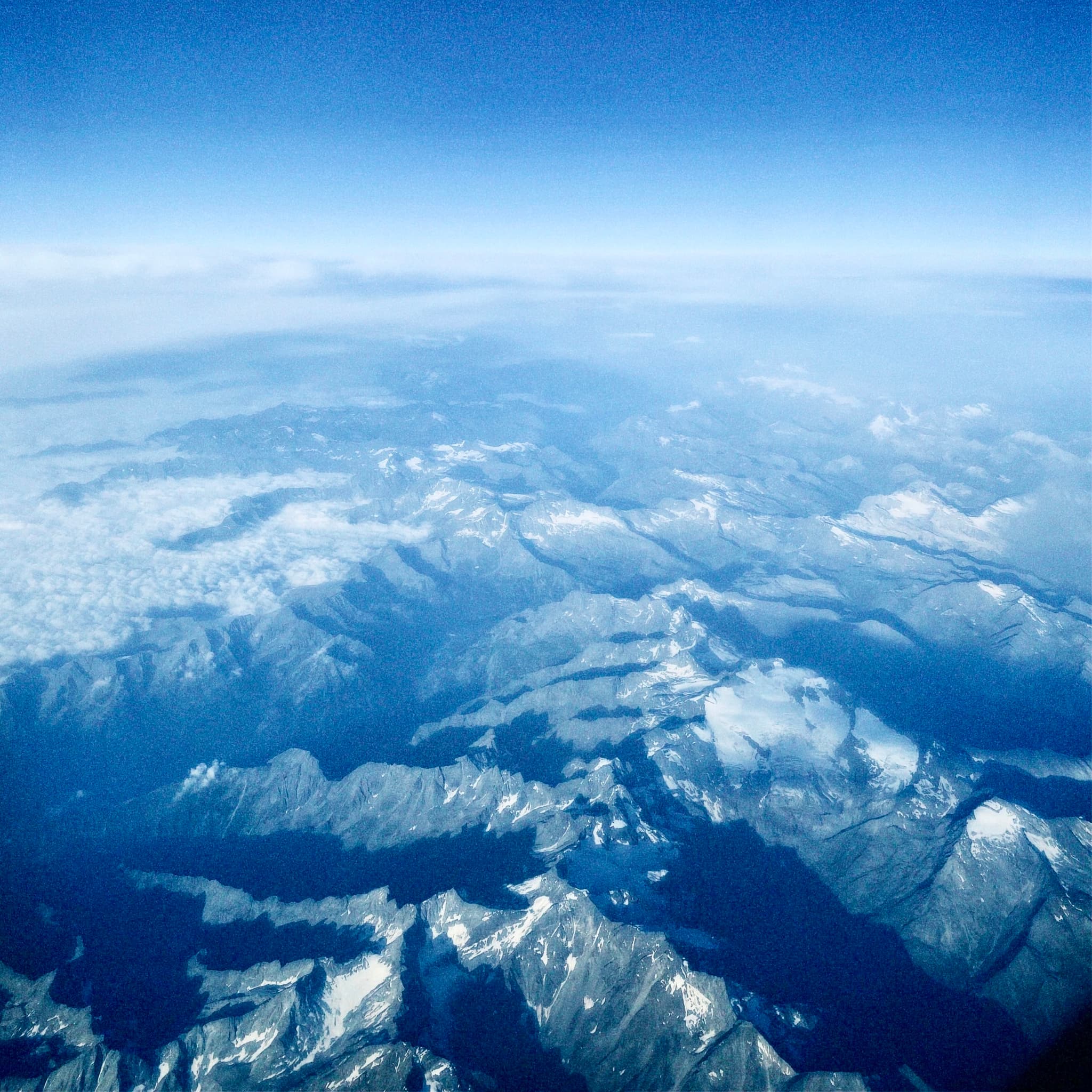 Spectacular aerial view of snow-capped mountains against a clear blue sky, bathed in natural daylight, evoking a serene and majestic atmosphere
