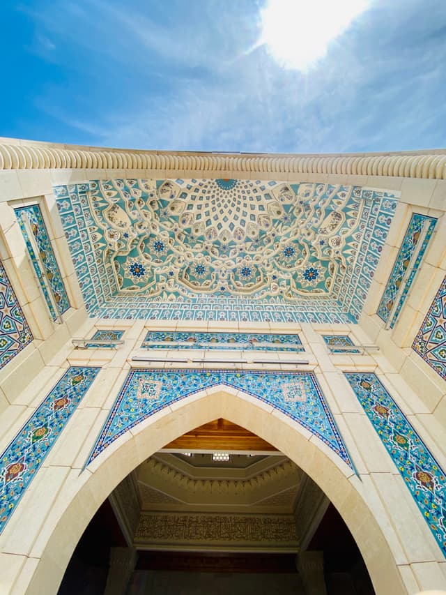 Illuminated by natural light, this stunning Islamic mosque interior features intricate blue and white mosaic tiles, a grand arch, and a clear blue sky above