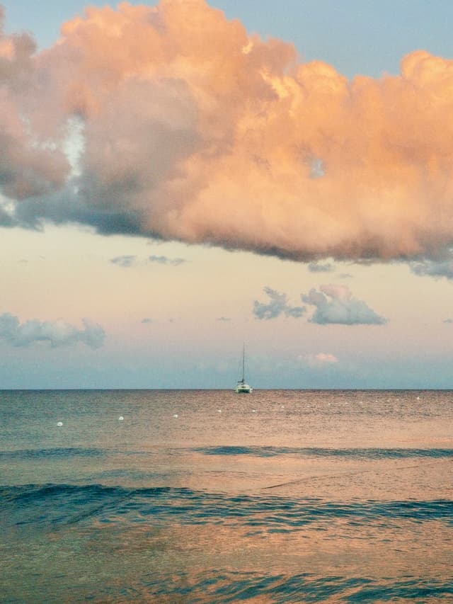 A serene sunset over the ocean, with a sailboat silhouetted against the sky, creating a tranquil and picturesque mood