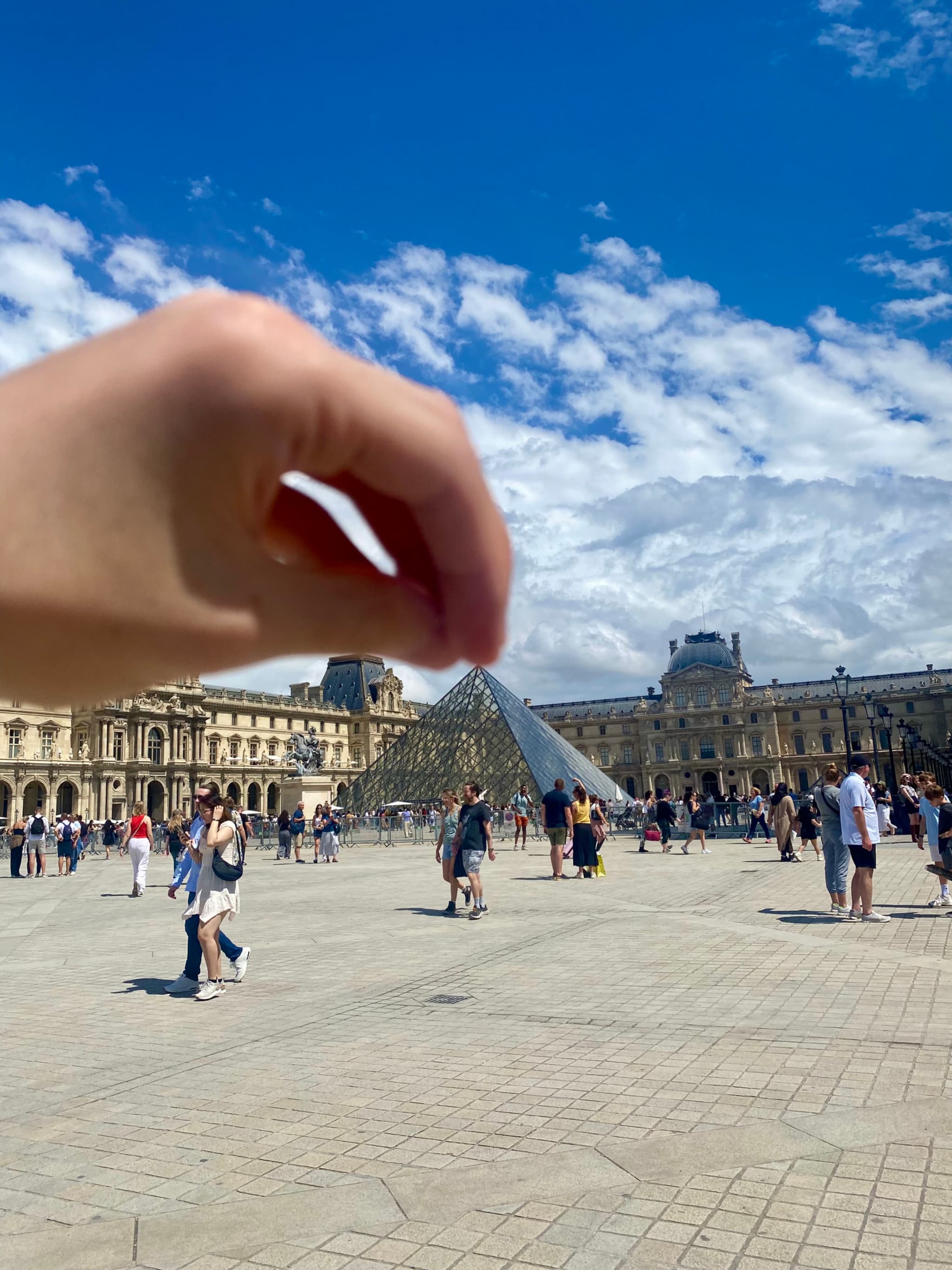 Tourists explore the Louvre's glass pyramid under a bright blue sky, with the historic museum in the background