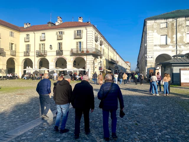 A bustling town square in the late afternoon, with historic architecture and people walking, bathed in warm, golden sunlight
