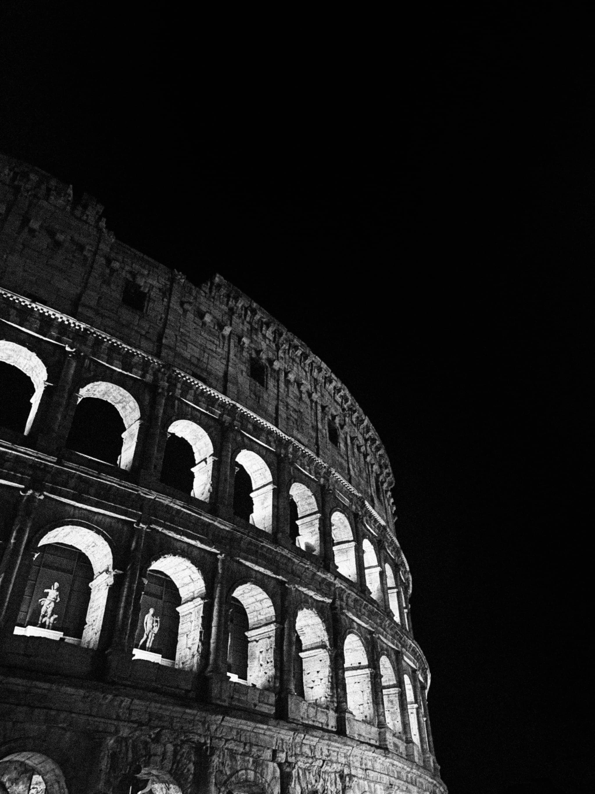 Illuminated Colosseum at night, dark sky, dramatic lighting highlights arches, evoking timeless grandeur